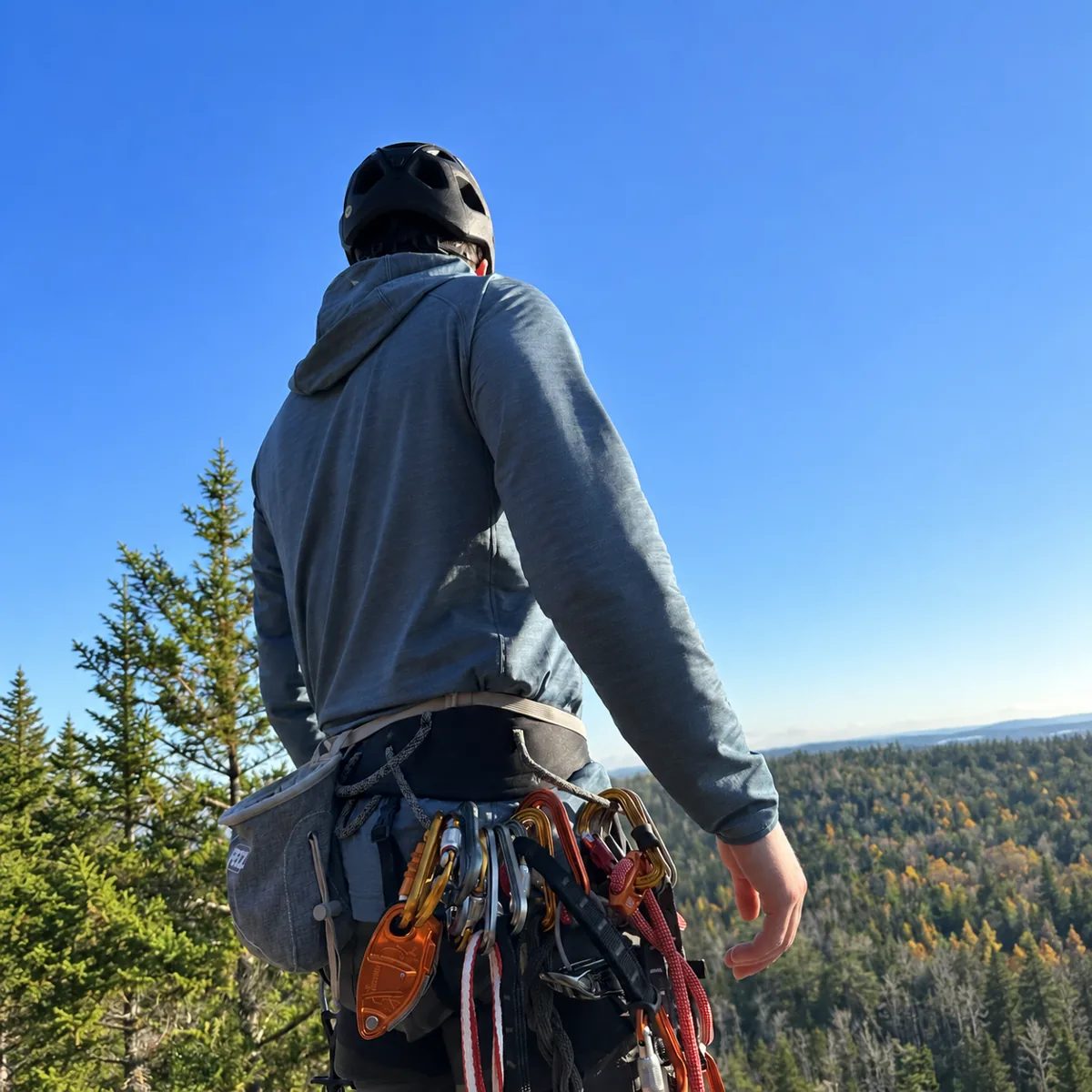 Mark wearing a climbing harness and helmet above the forest