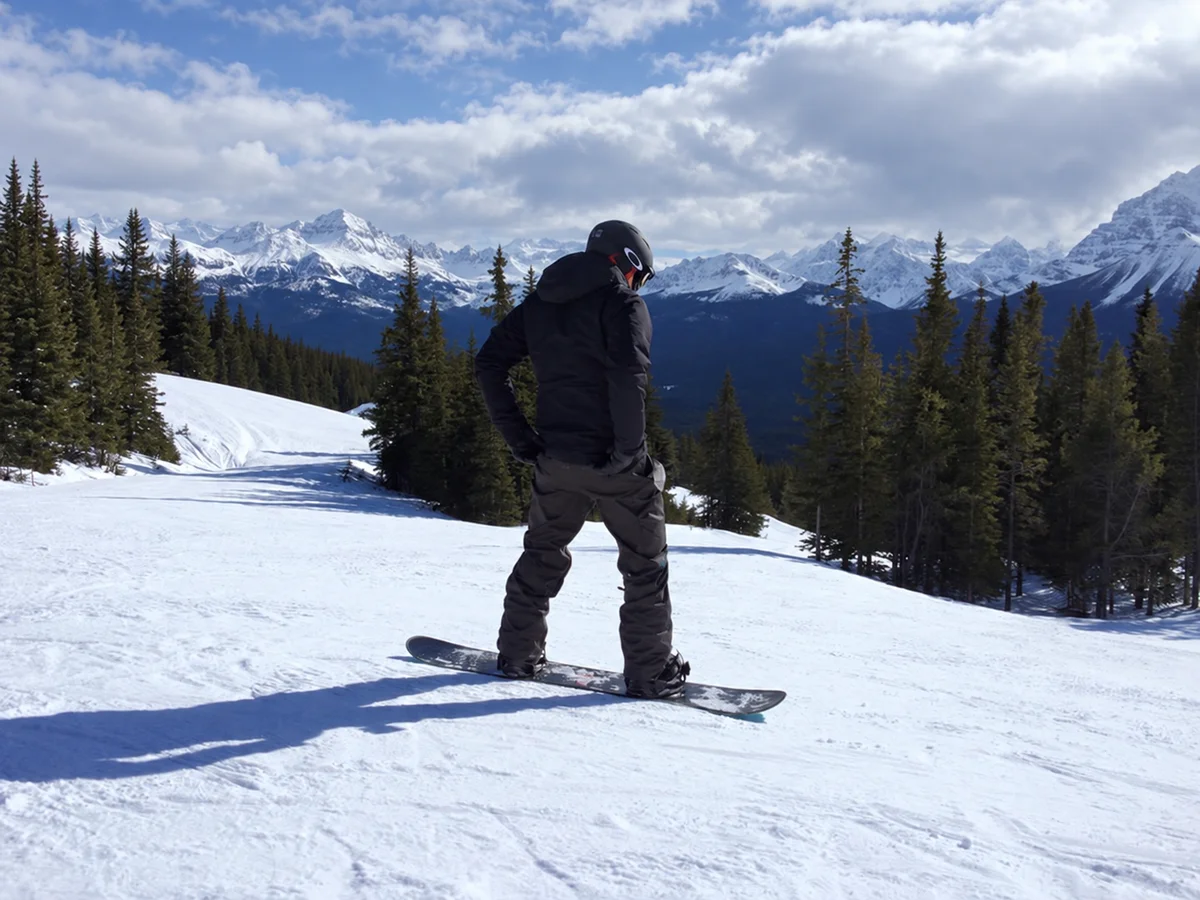 Mark on a snowboard overlooking forest and snow-covered mountains